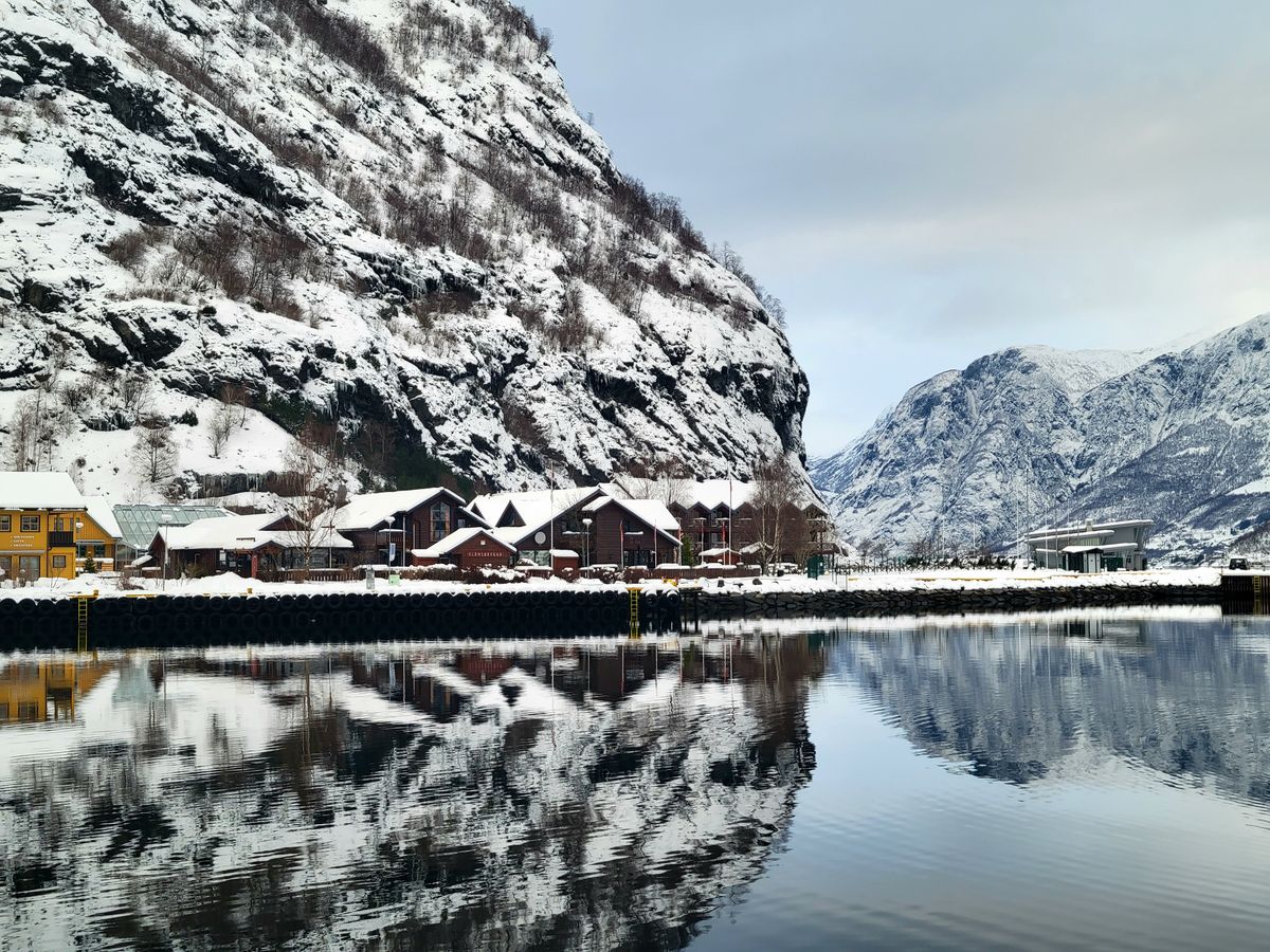 Winter scene of Flam village with fjord reflections and snow-covered mountains