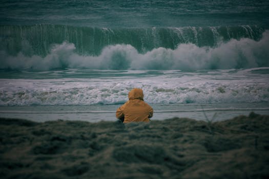 Person in a yellow jacket sitting on a beach, watching the ocean waves crash in autumn.
