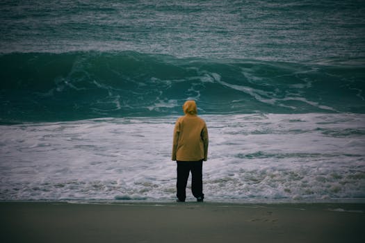 A person in a yellow raincoat stands alone by the ocean in Nouvelle-Aquitaine, France.