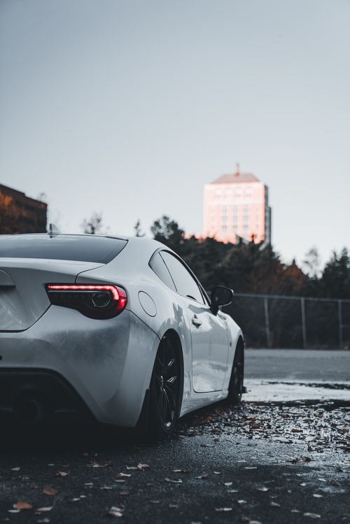 Free A white sports car parked in a city with a distant skyscraper, embodying urban elegance. Stock Photo