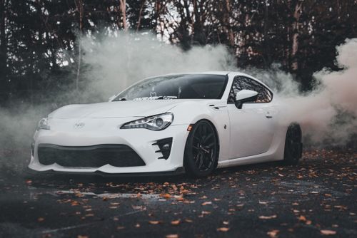 Free A sleek white sports car drifting through smoke on a leaf-covered road in autumn. Stock Photo