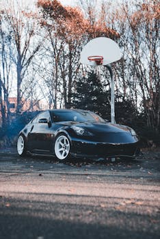 A sleek black sports car parked on a basketball court surrounded by autumn trees.