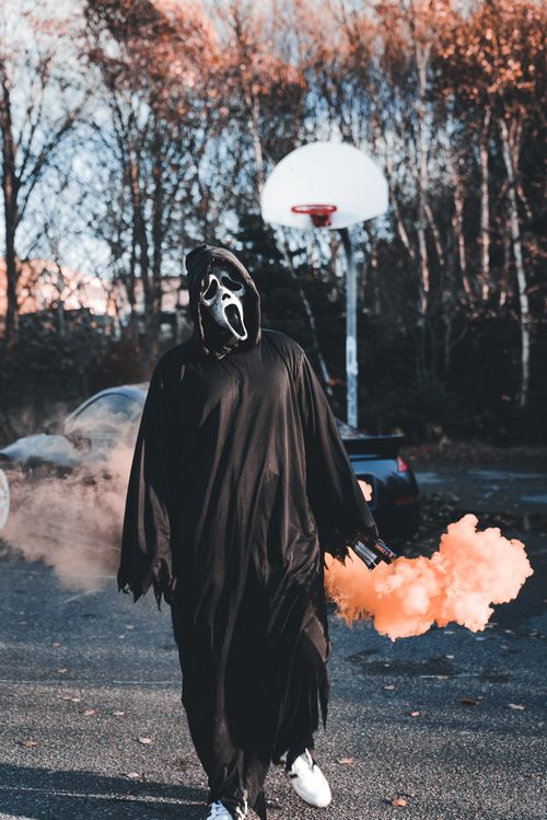 Free A person in a ghost costume holds smoke bomb on outdoor court. Stock Photo