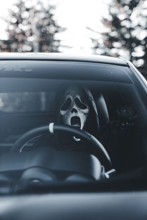 Free A person wearing a ghost mask behind the wheel of a car in a creepy setting. Stock Photo