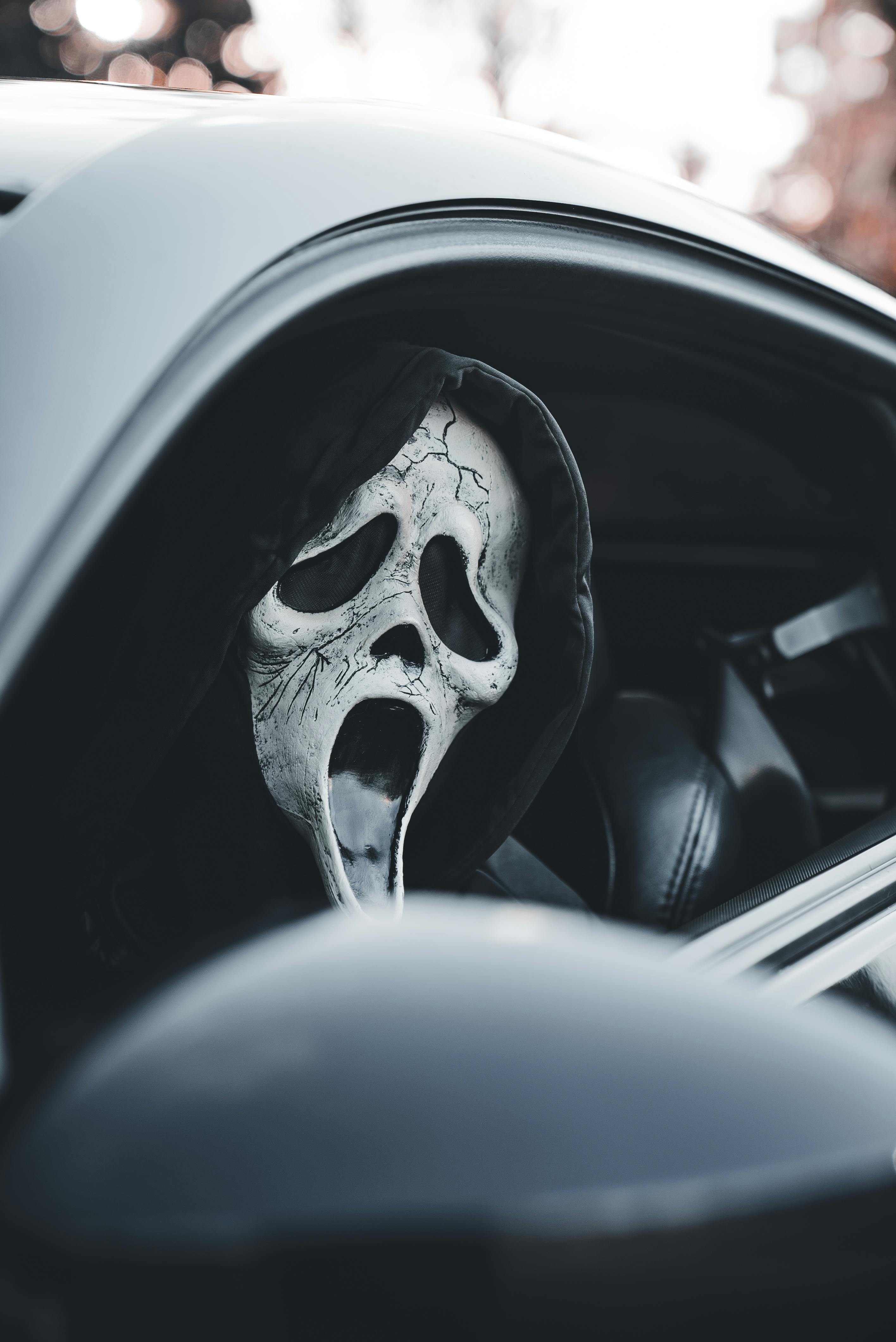A chilling ghost face mask peeks from a car window, evoking a sense of Halloween thrill.