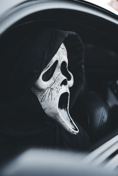 Free Person wearing iconic scream mask looks out car window, capturing a spooky Halloween vibe. Stock Photo