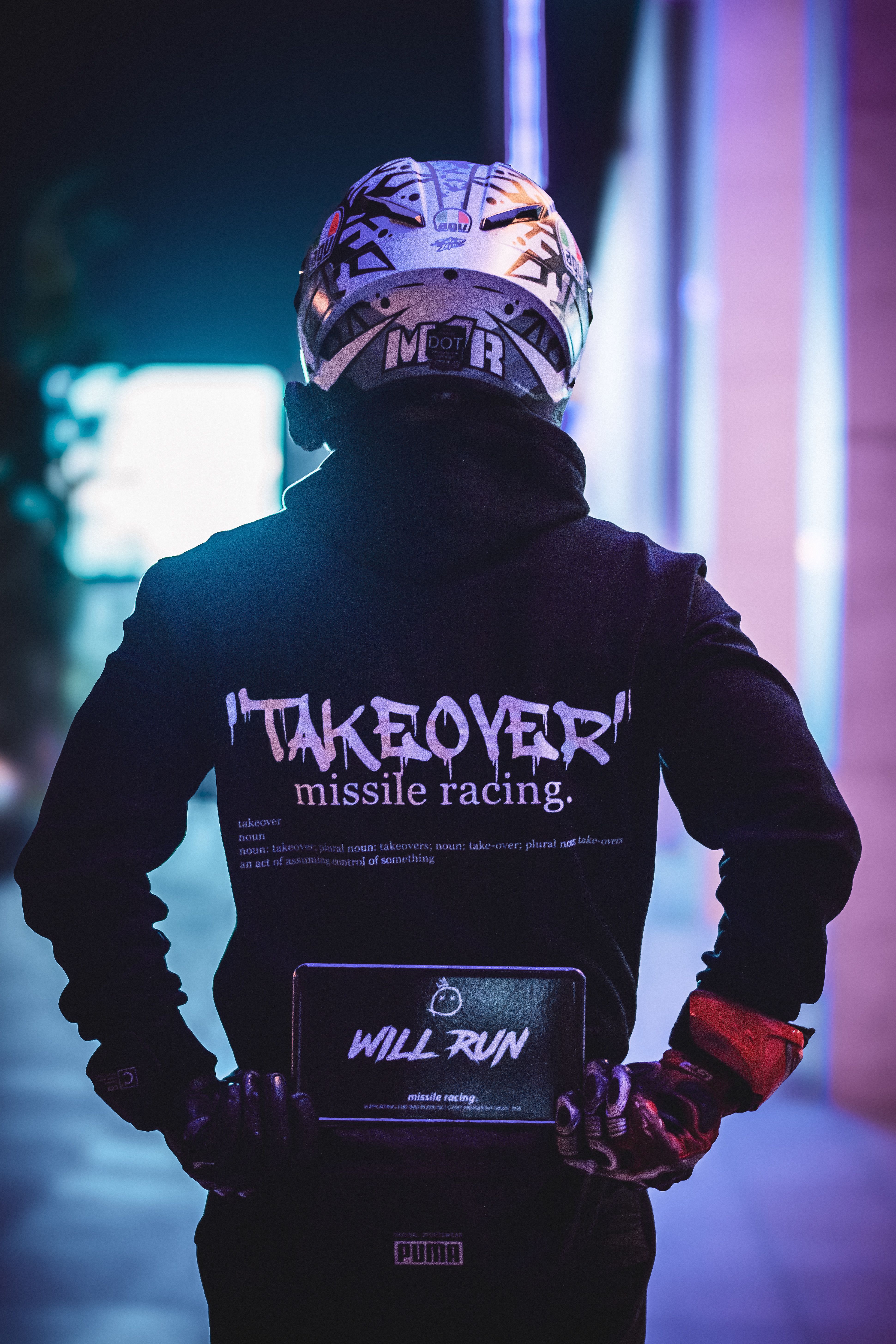 Rider in helmet and streetwear facing away, night urban scene.