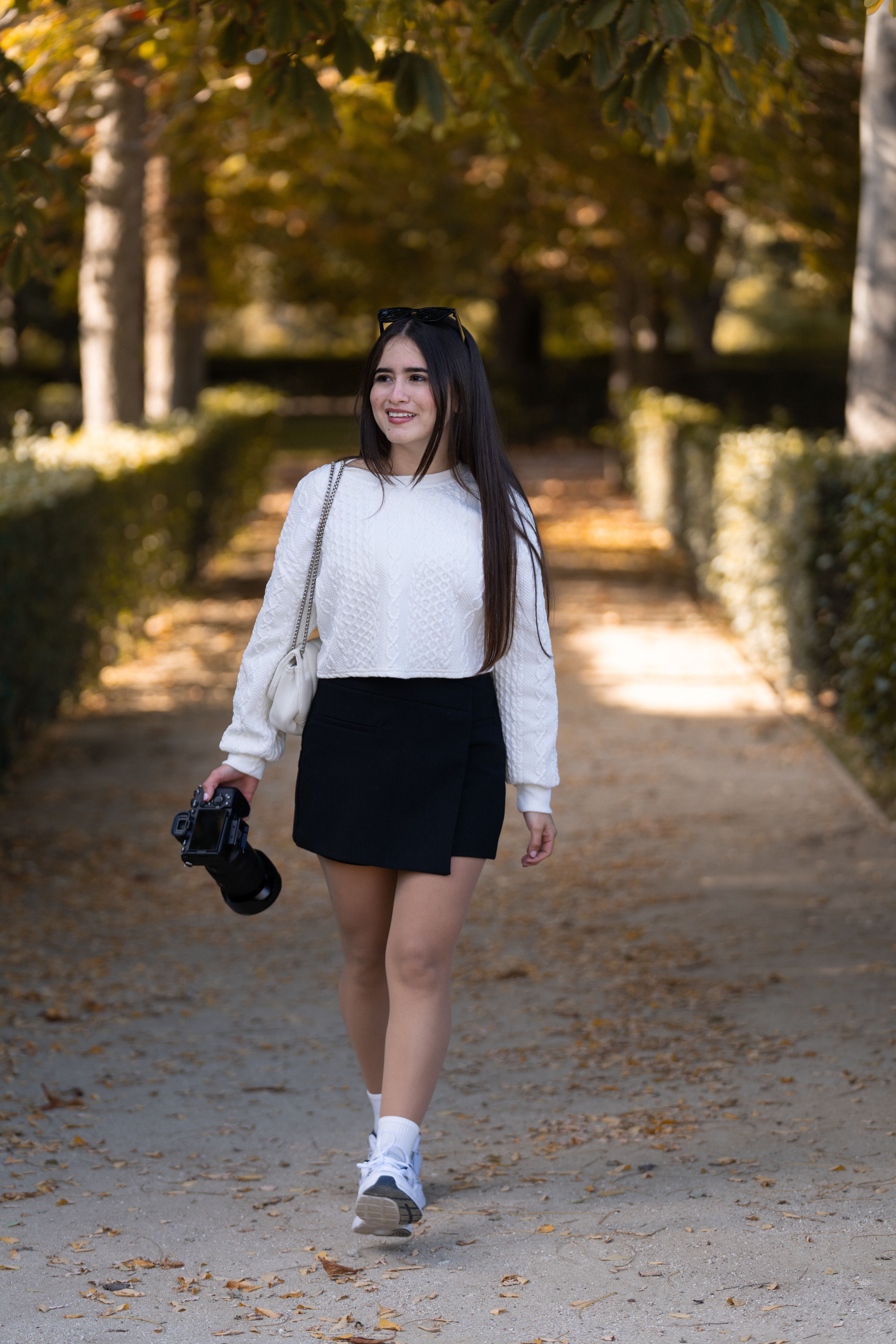 Young woman walking with a camera in a leafy park in Madrid, Spain during fall.