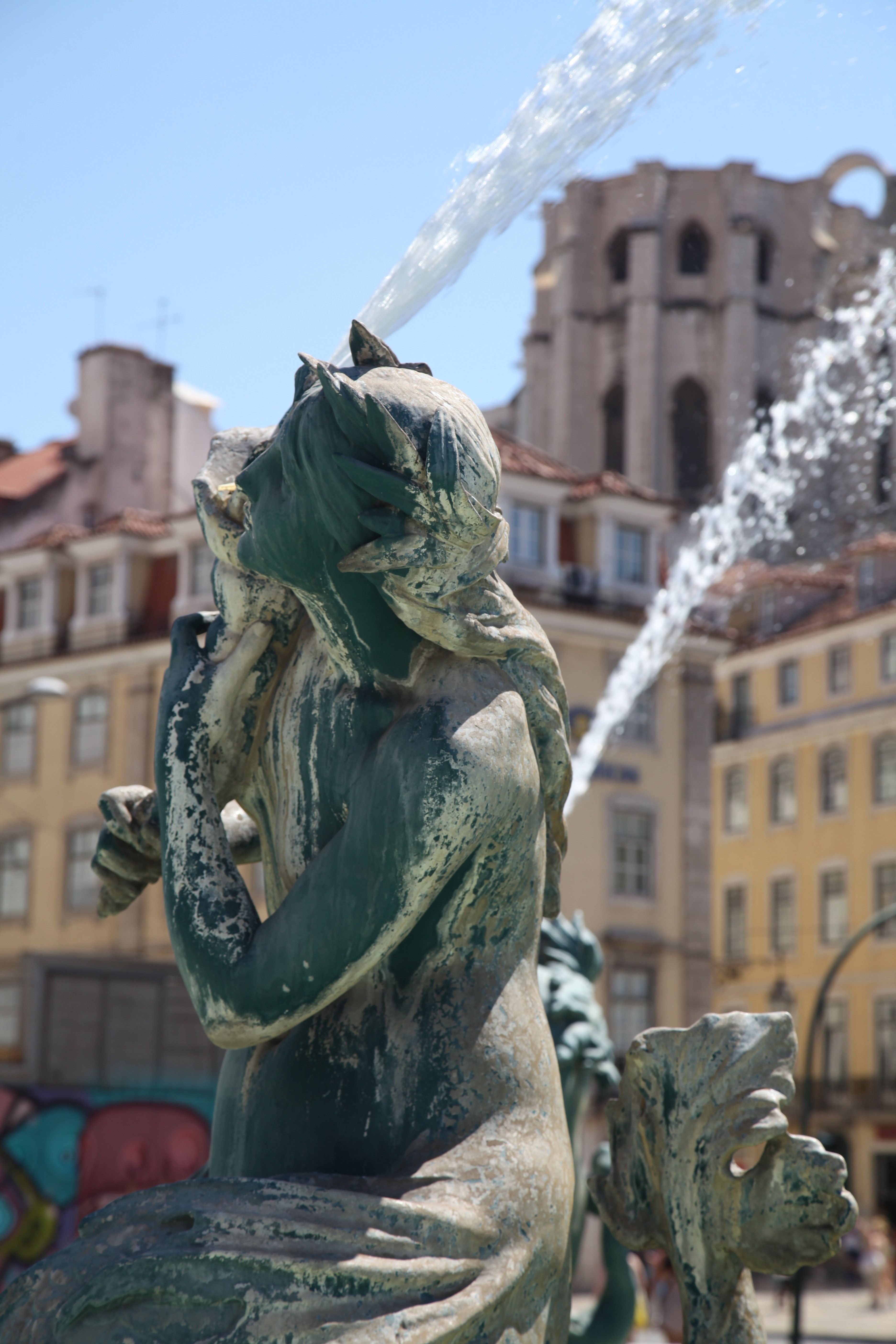 Beautiful fountain sculpture in Lisbon with historic buildings in the background on a sunny day.