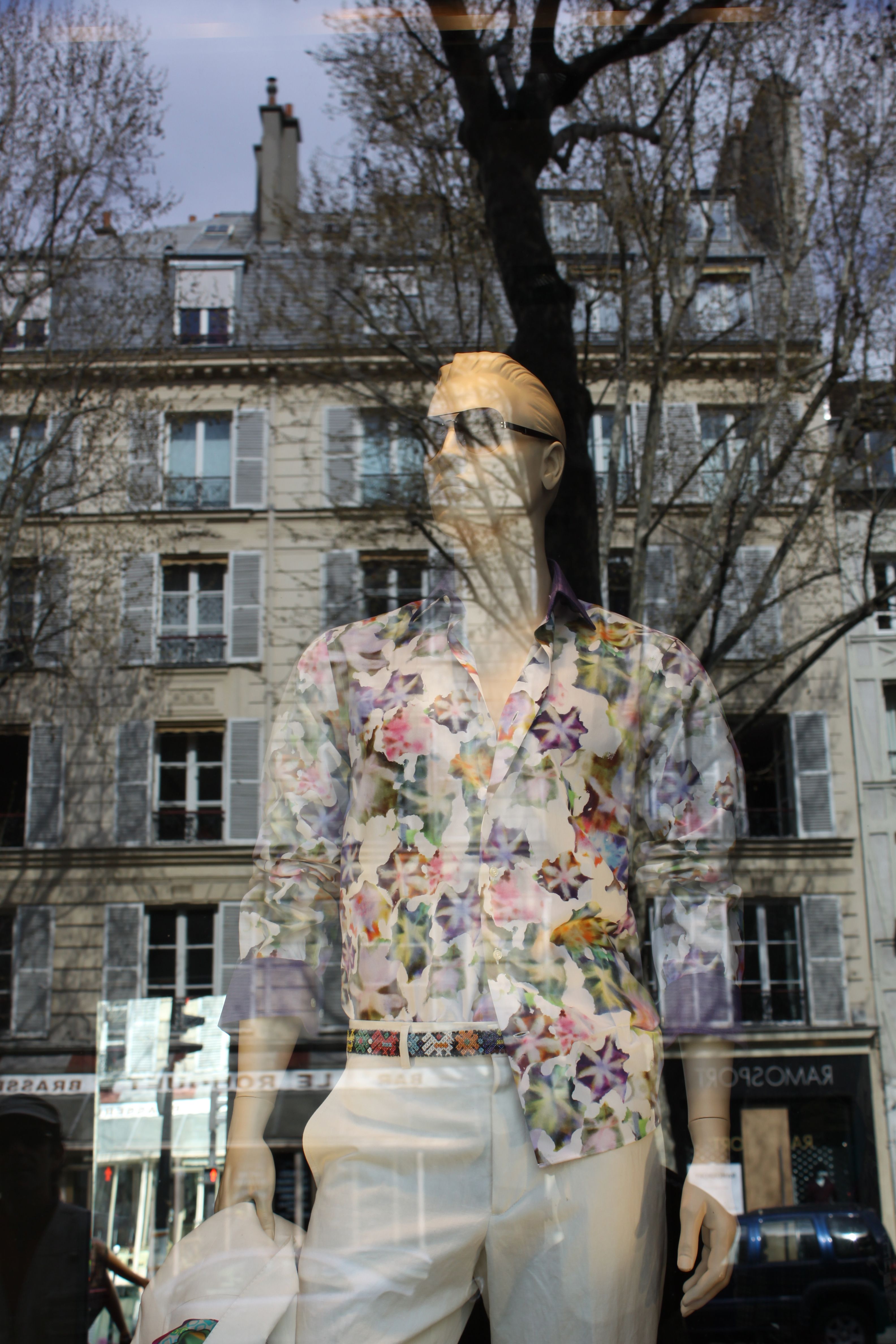 Mannequin in vibrant floral shirt, Parisian building reflection.