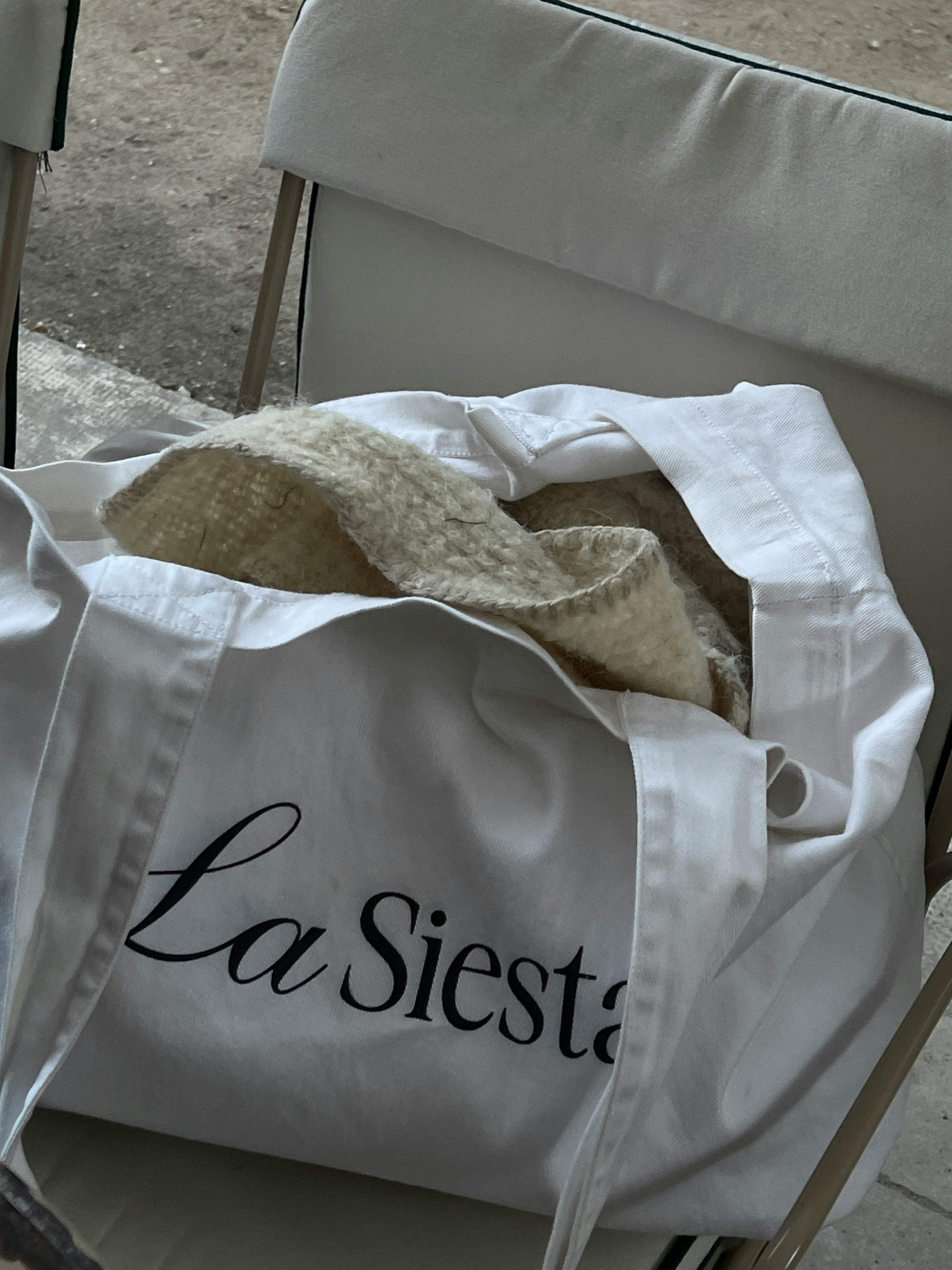 A white 'La Siesta' bag on a beige chair, holding a cozy blanket.