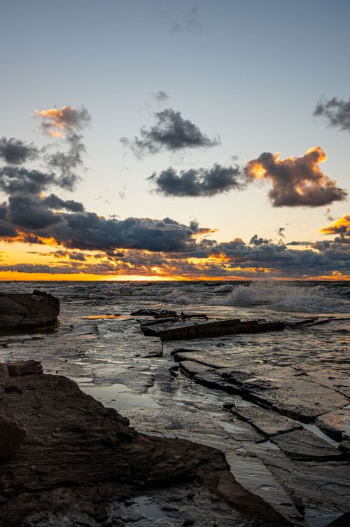 Free Stunning sunset over a rocky shoreline with vibrant clouds and waves crashing. Stock Photo