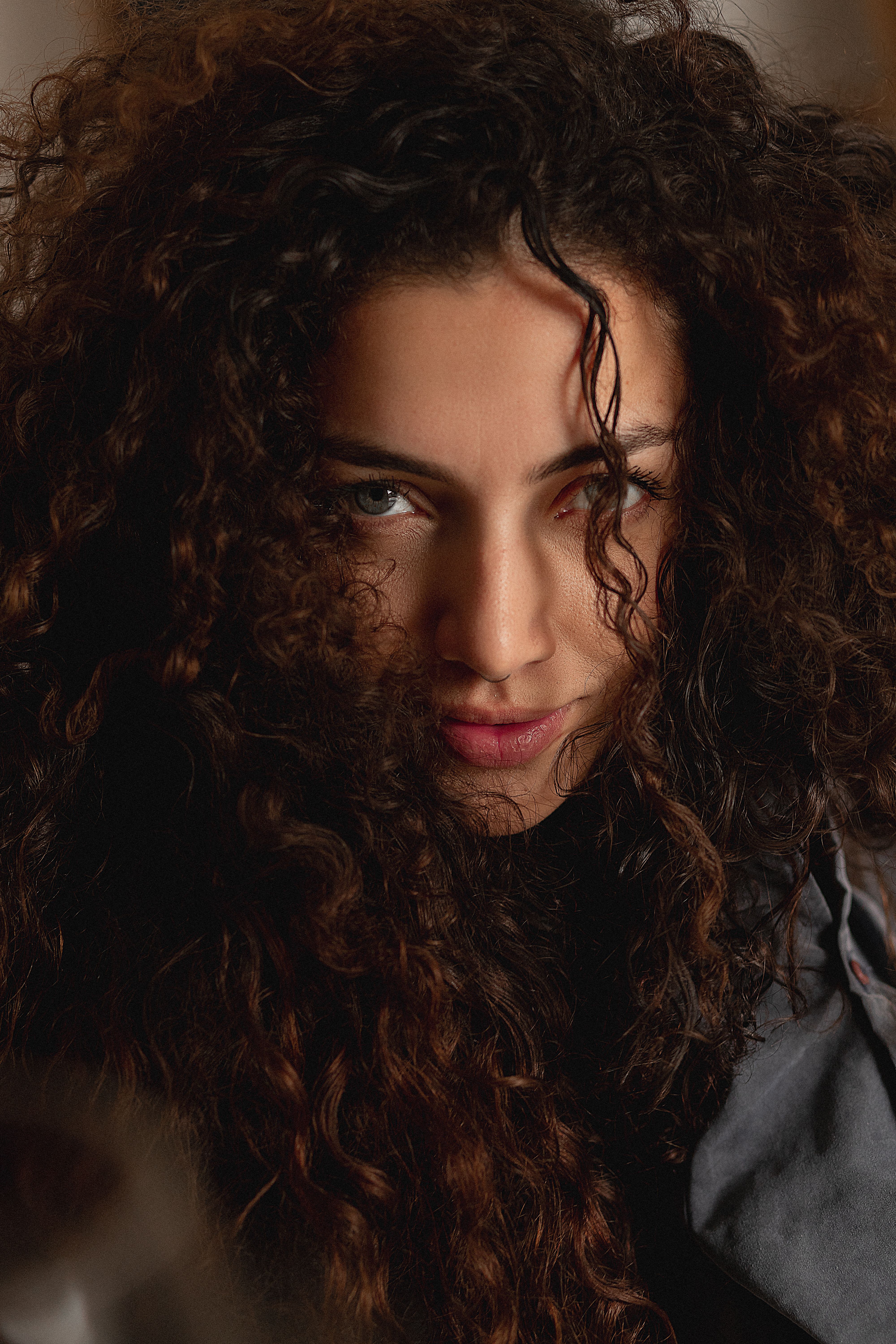 Close-up portrait of a woman with thick curly hair and intense gaze, indoors.
