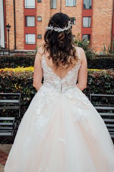 Bride standing in beautiful lace gown with floral headpiece, facing lush garden backdrop.