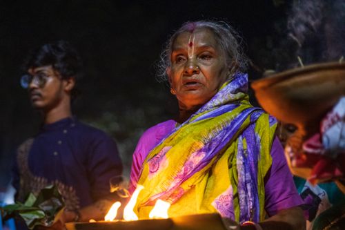 Free Elderly woman participates in a night-time Indian religious ceremony with offerings and fire. Stock Photo