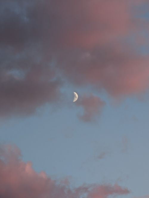 Free A half moon amidst pink clouds set against a serene blue evening sky. Stock Photo