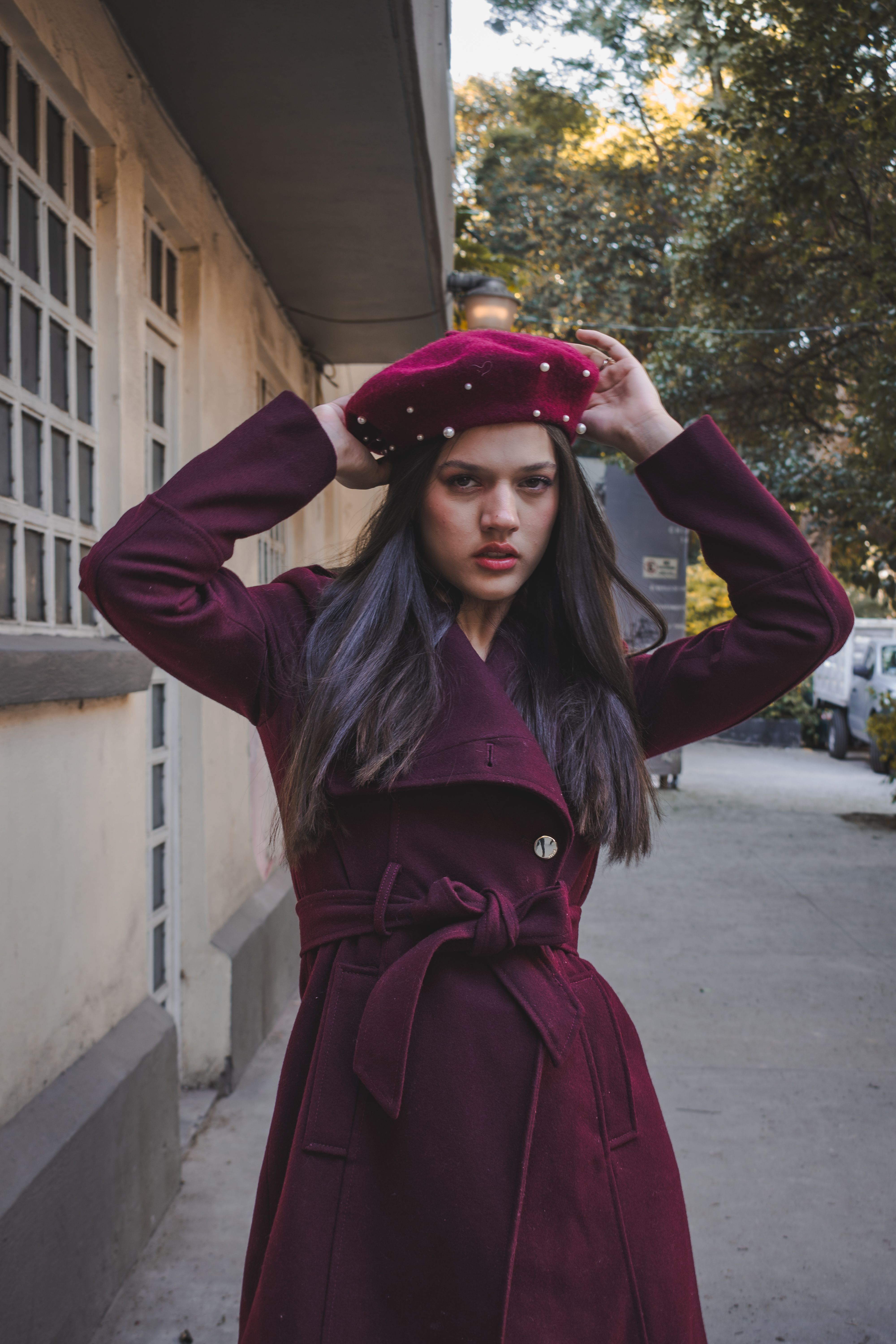 Fotomural Mujer elegante con abrigo burdeos y sombrero posando al aire libre en un entorno urbano.