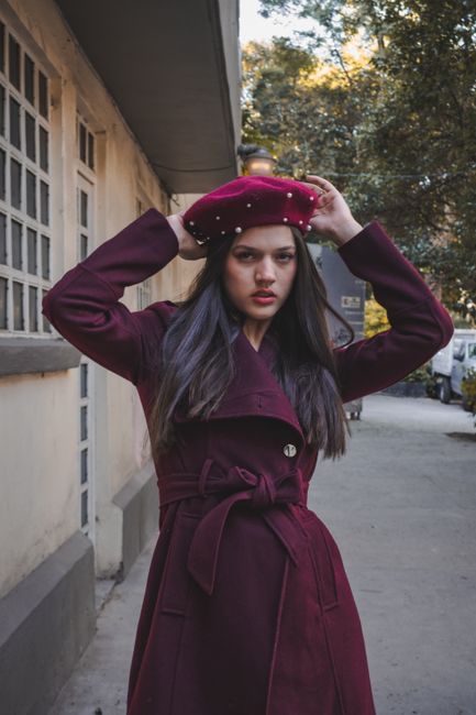 Fotomural Mujer elegante con abrigo burdeos y sombrero posando al aire libre en un entorno urbano.