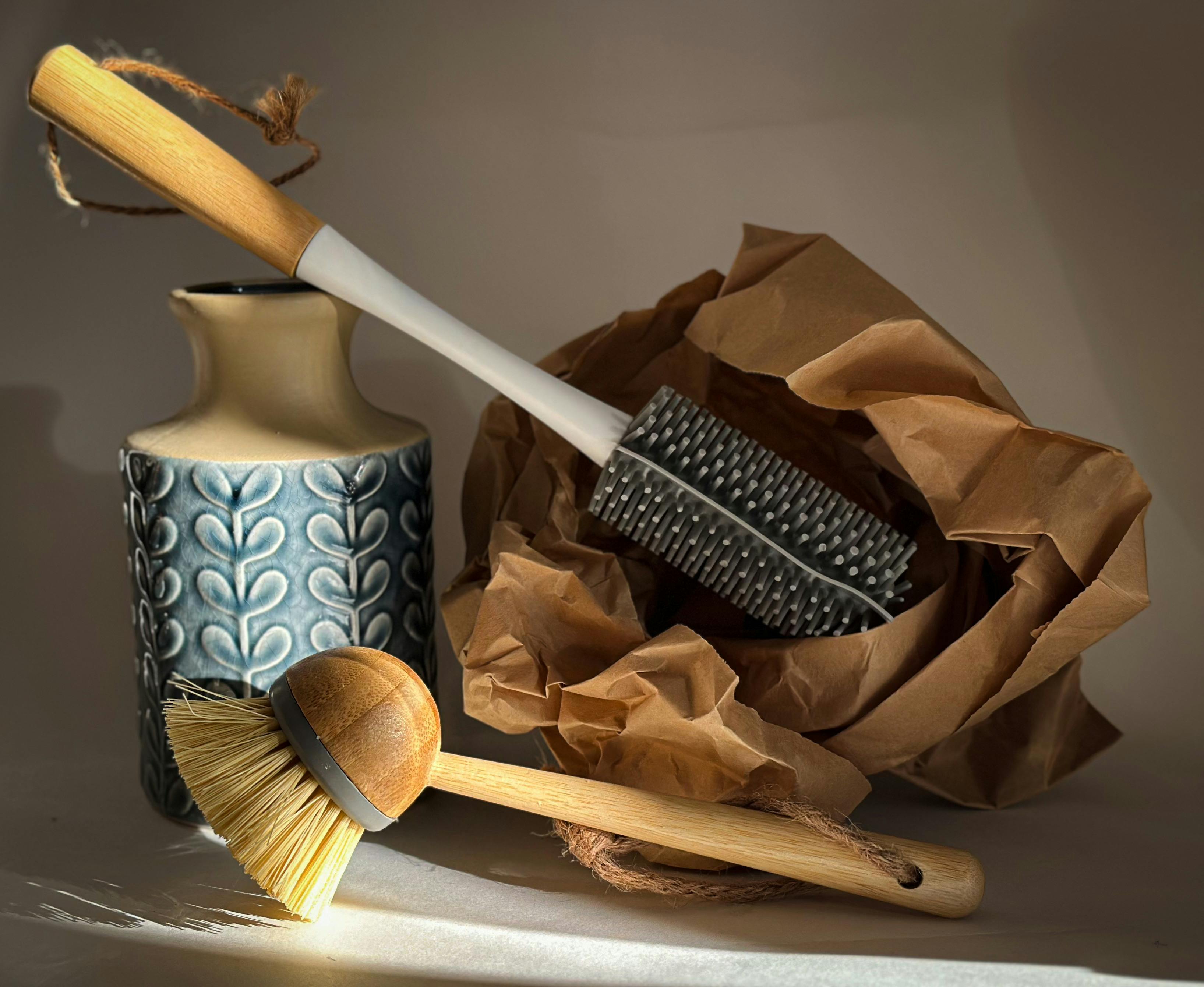Stylish still life of eco-friendly cleaning brushes, a textured ceramic vase, and crumpled brown paper.