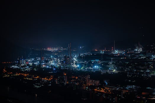 A vibrant cityscape of industrial buildings glowing against the dark night sky.