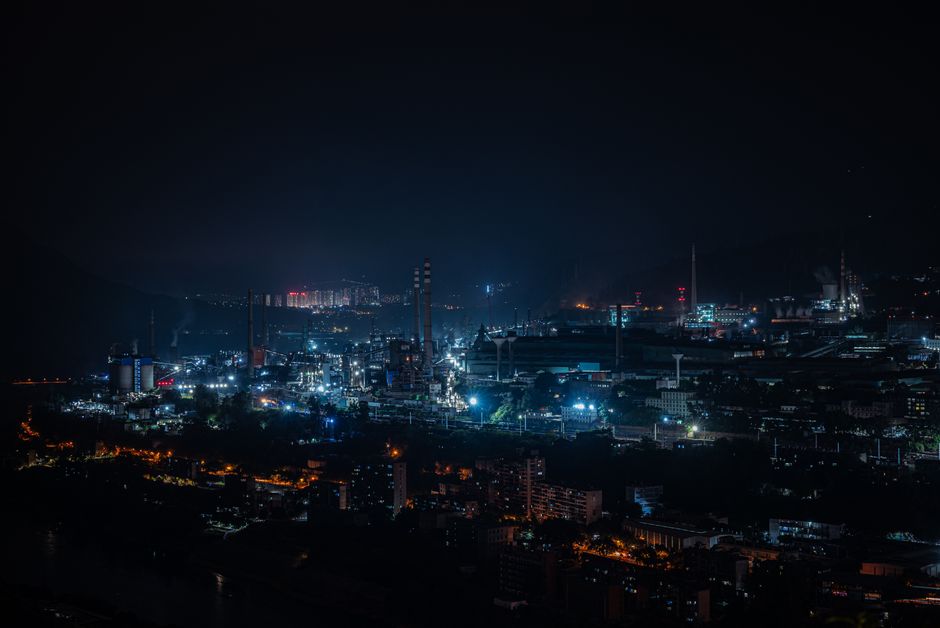 A vibrant cityscape of industrial buildings glowing against the dark night sky.