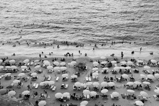 Aerial shot of people enjoying a lively beach day with umbrellas and waves.