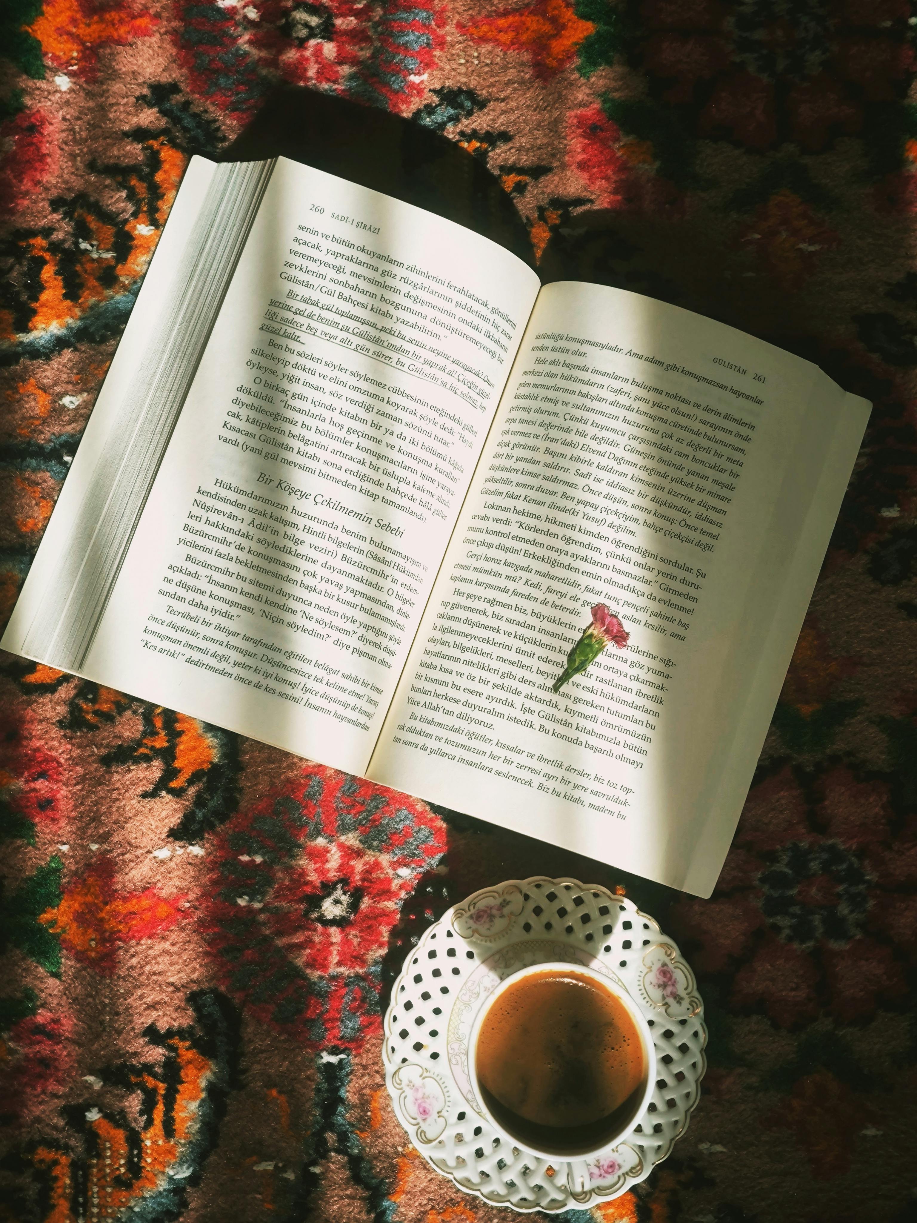 Open book with a flower petal and a cup of coffee on an ornate carpet.