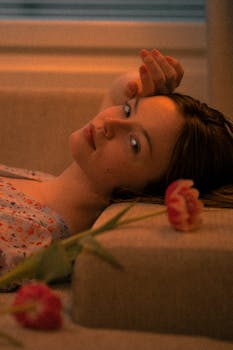 Artistic portrait of a young woman lying with tulips in a warm, ambient setting.