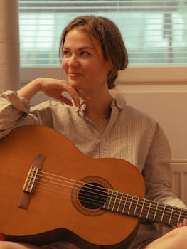 A relaxed young woman with an acoustic guitar enjoying a peaceful moment indoors.