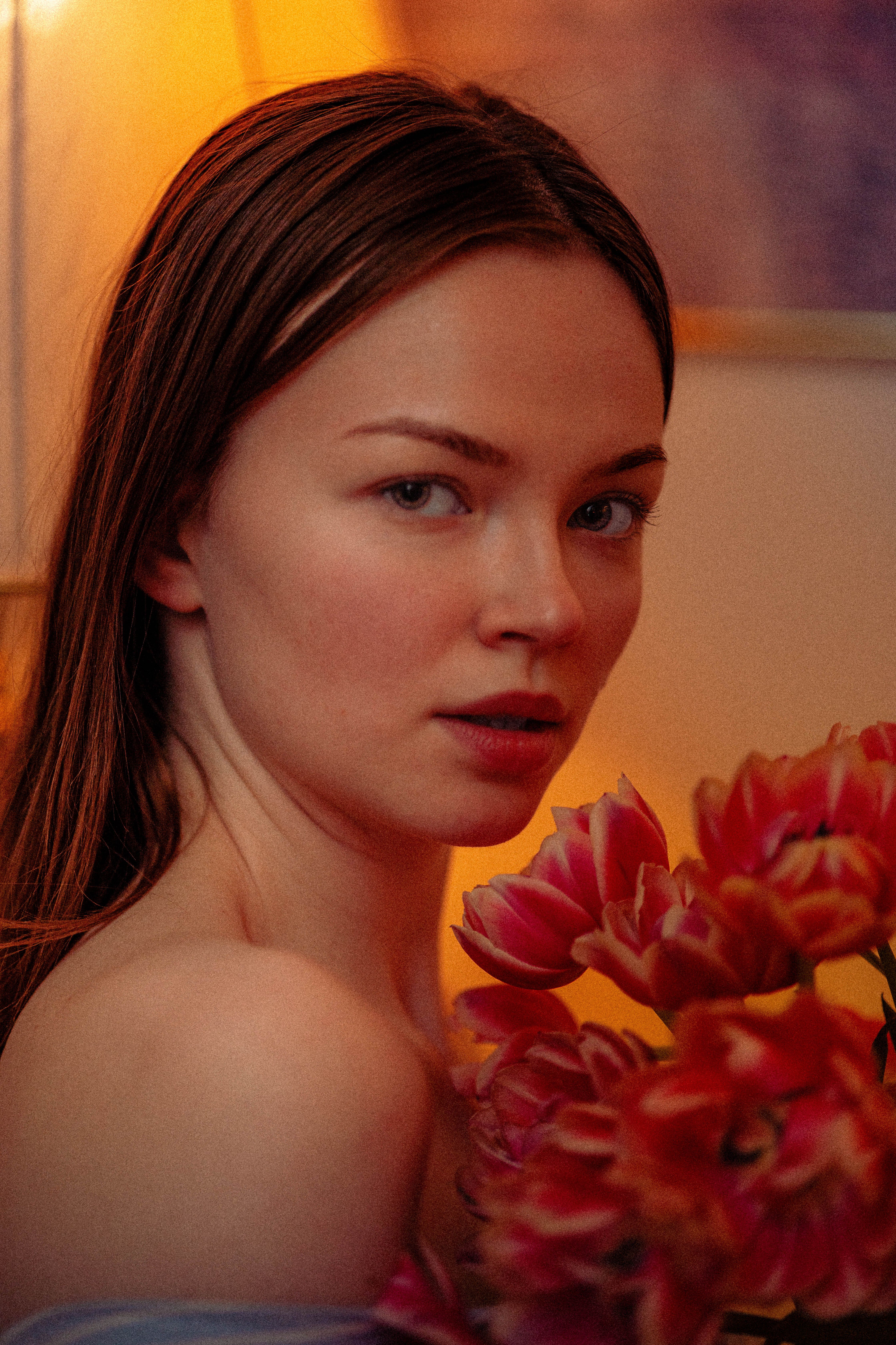 Elegant portrait of a young woman holding vibrant tulips indoors with warm lighting.