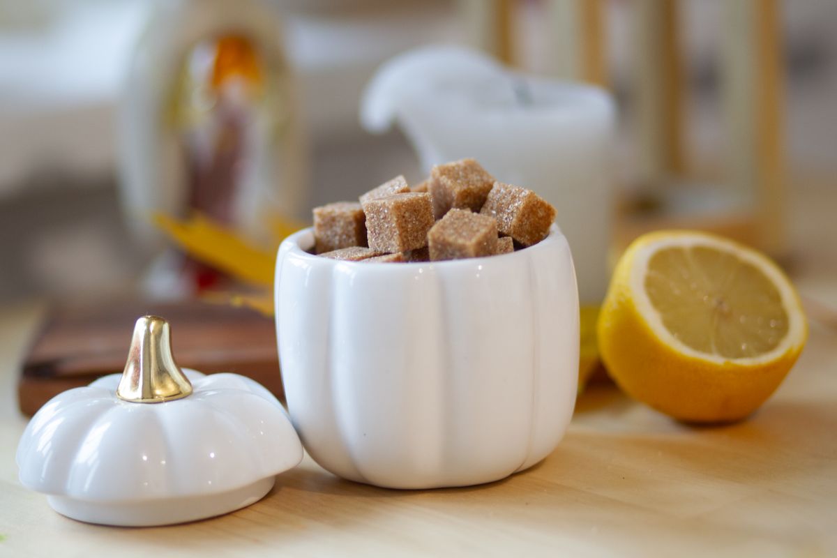 White ceramic container with sugar cubes and sliced lemon on kitchen table.