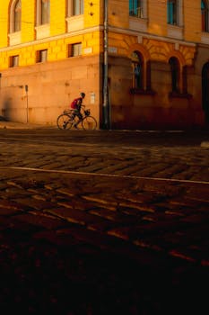 A cyclist rides past a historic Helsinki building, bathed in warm evening light.