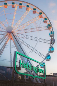 Illuminated ferris wheel in Helsinki during evening with a glowing sign.