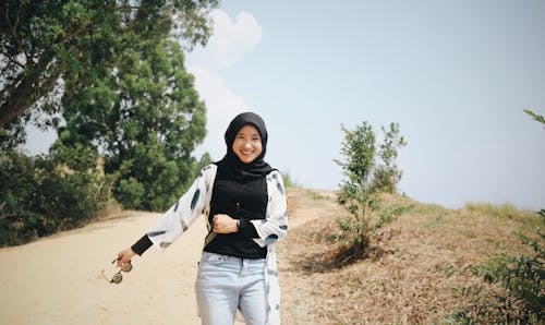 Photo of Smiling Woman in Black Hijab Standing on Dirt Road