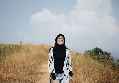비포장 도로 한가운데 서있는 검은 히잡에 웃는 여자의 사진