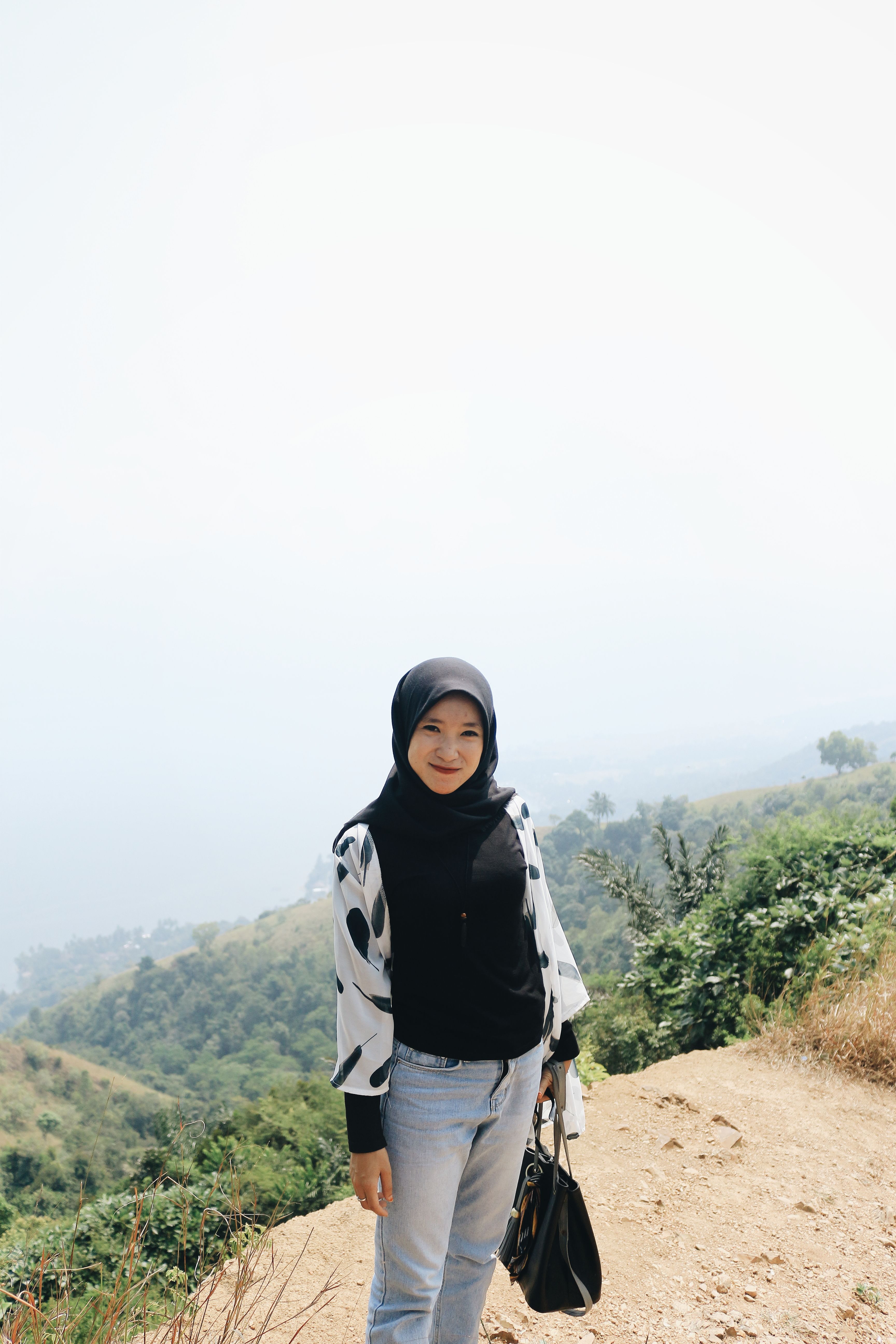 Content Asian female in headscarf looking at camera while standing on edge of cliff with foggy nature on background
