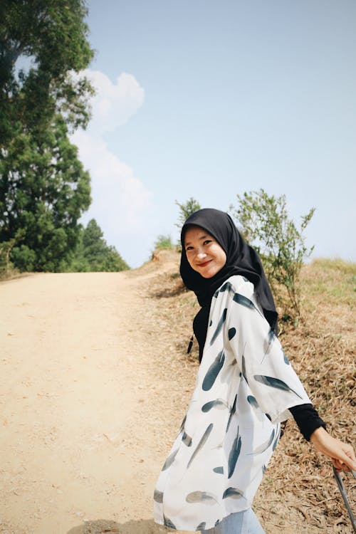 Foto De Uma Mulher Sorridente Em Um Hijab Preto Em Uma Estrada De Terra, Olhando Para Trás