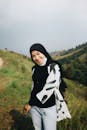 一位开朗的女子戴着头巾，在长满草的户外山顶上快乐地摆姿势