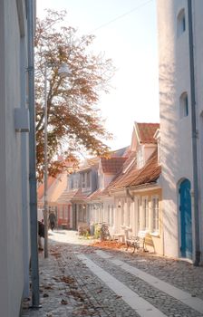 A picturesque European street with fall colors and sunlight casting shadows.