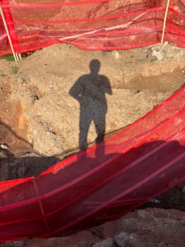 Shadow of a person on earth surrounded by red construction barriers.