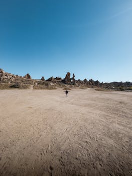 A solitary person stands in a wide open desert with unique rock formations under a clear blue sky.