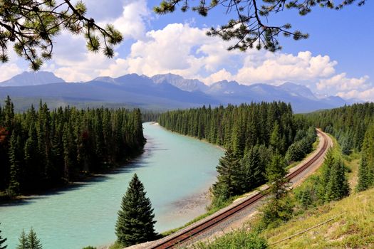 Idyllic summer landscape featuring a river, railway, and mountains.