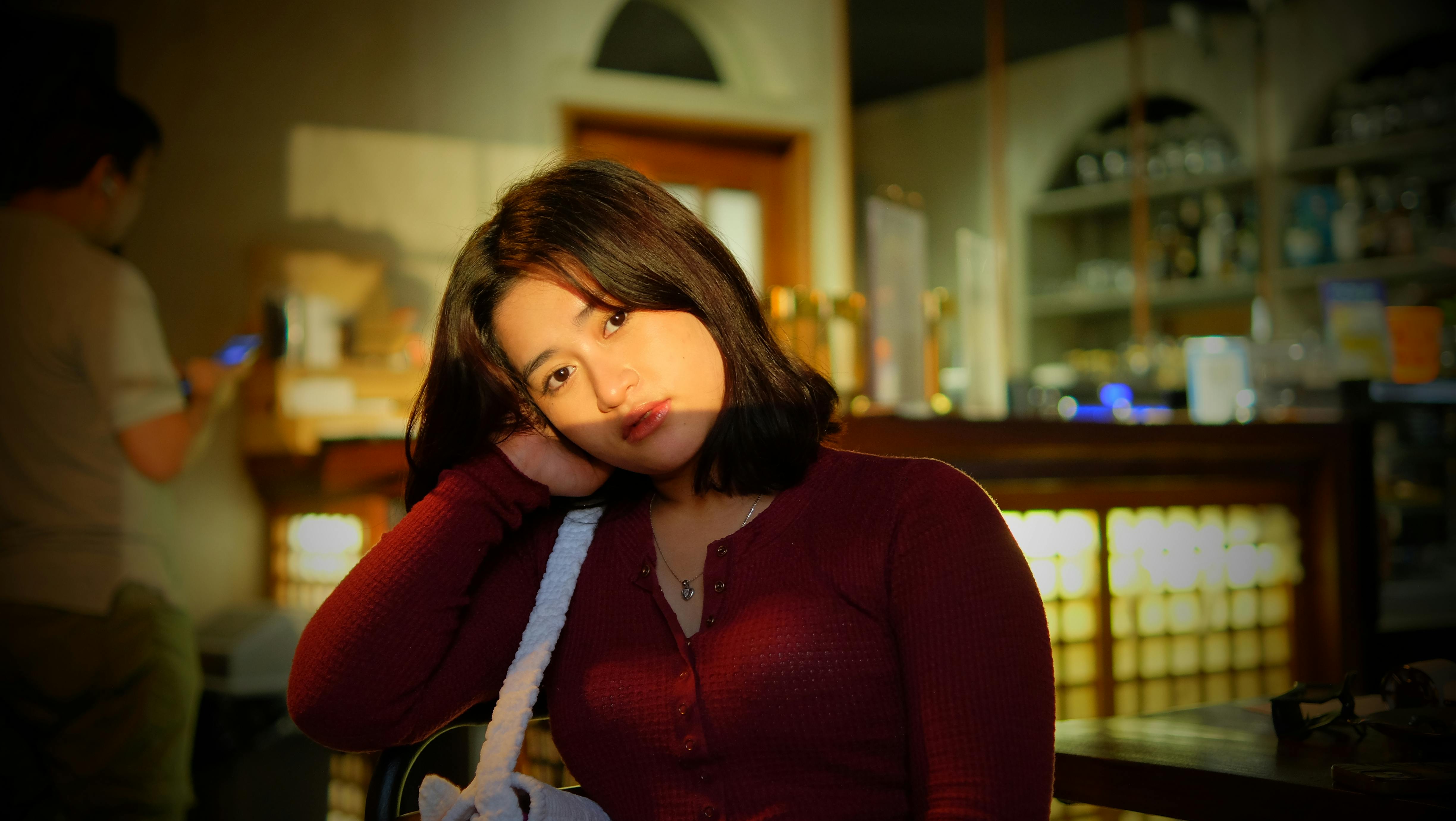 Kostenlos Porträt einer jungen Frau in einem Innenbereich mit warmer Beleuchtung in einer entspannten und gemütlichen Café-Atmosphäre. Stock-Foto