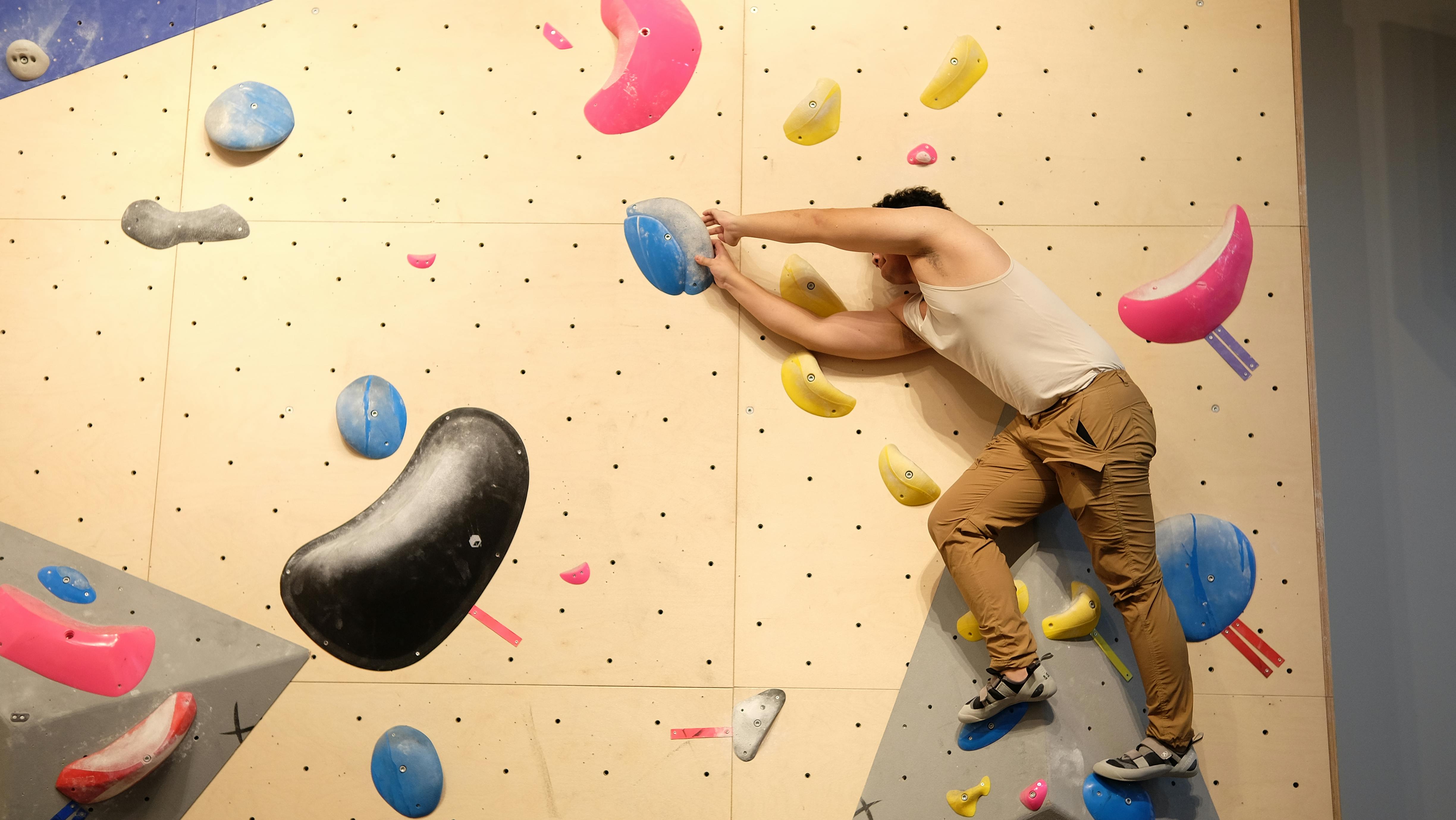Adult male climber scaling an indoor bouldering wall with colorful holds.