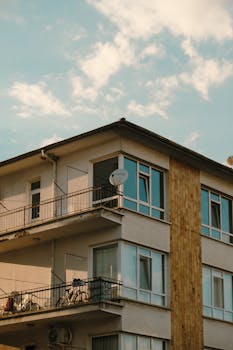 A modern apartment building with balconies under a blue sky featuring scattered clouds.