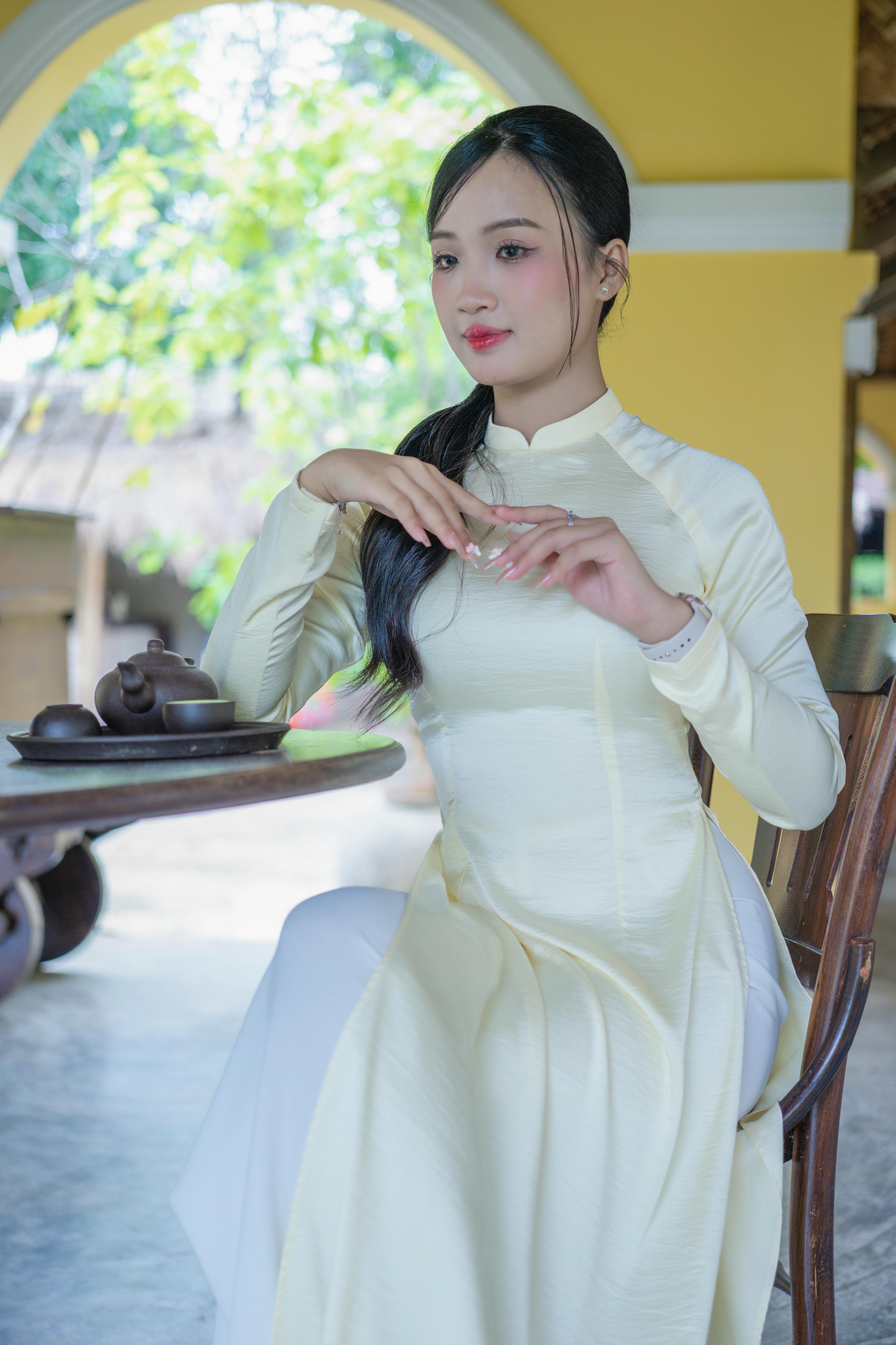 Portrait of a woman in a Vietnamese Ao Dai enjoying tea indoors.
