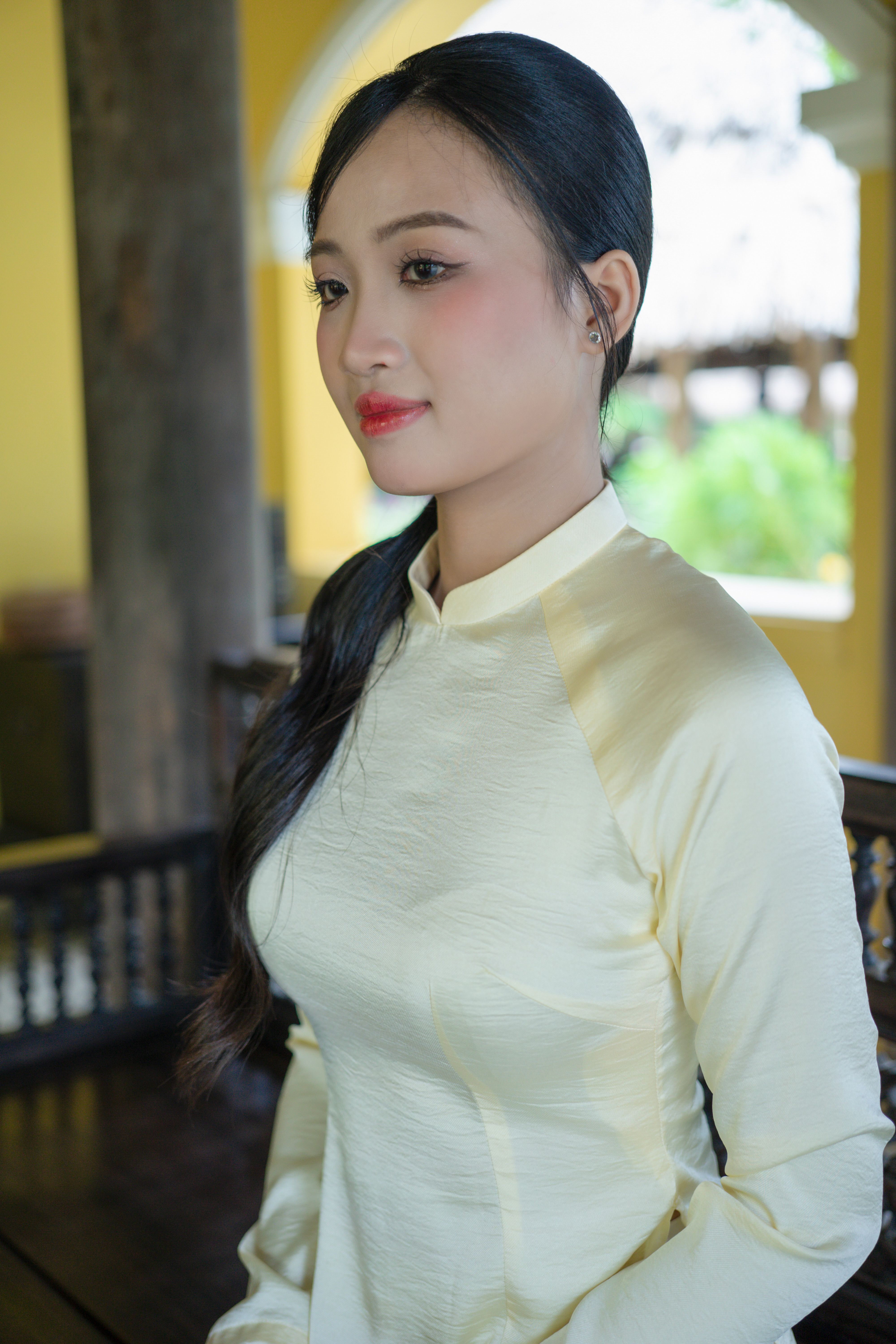 A young woman gazes gracefully, wearing a traditional Vietnamese Ao Dai indoors.