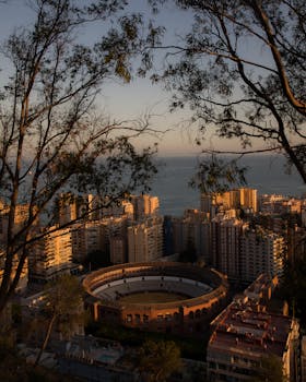 Captivating sunset view of Málaga cityscape featuring the historic Plaza de Toros with the sea in the background.