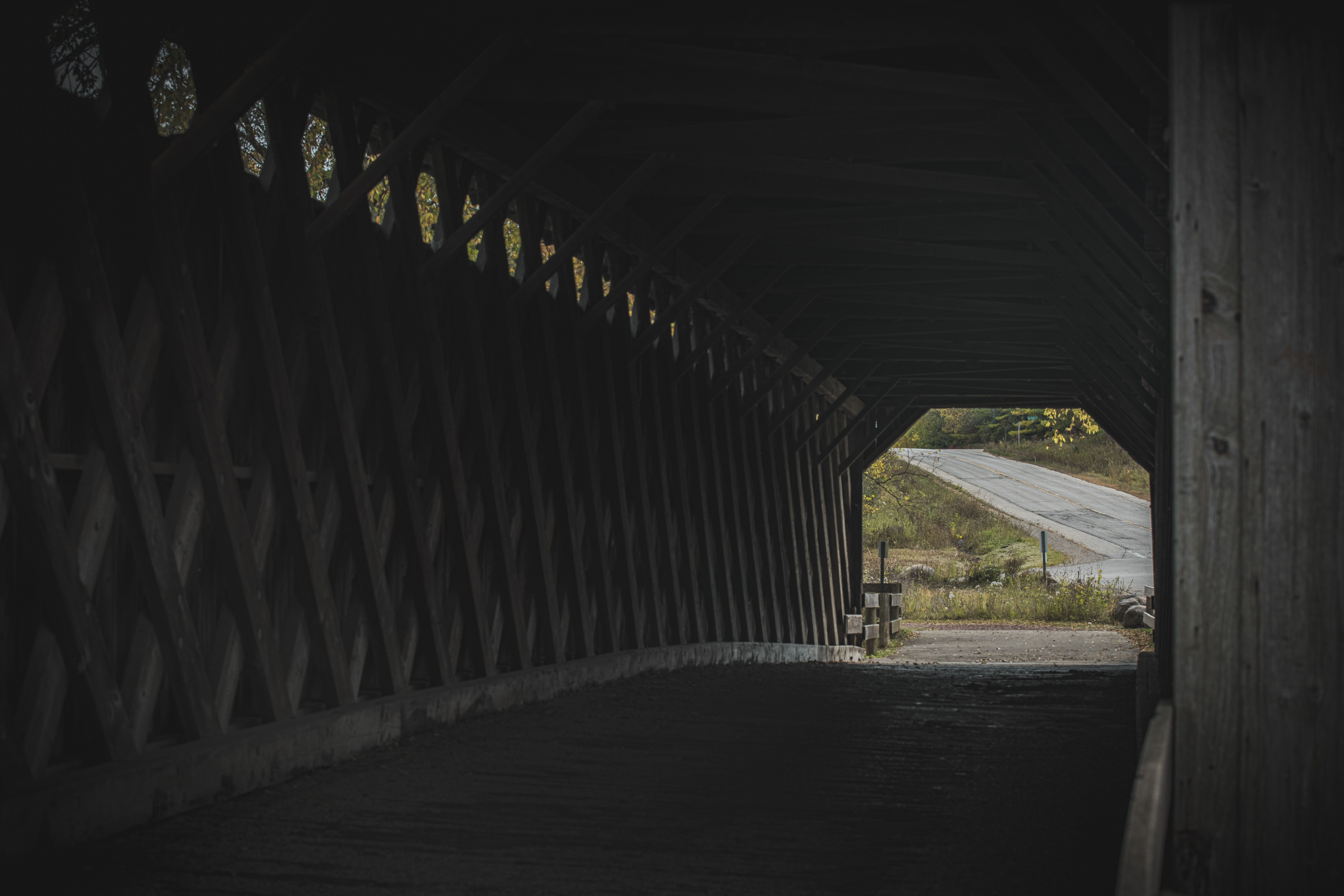 A dimly lit view through a wooden covered bridge with lush scenery.