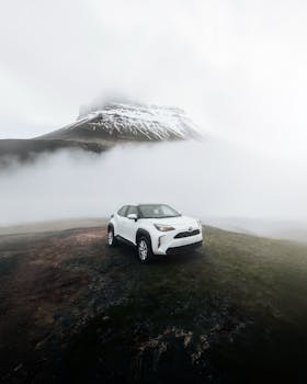 A sleek white SUV parked amidst a foggy mountain landscape with snow-capped peaks.